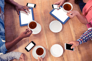 Colleagues using technologies at desk while holding coffee cups in office