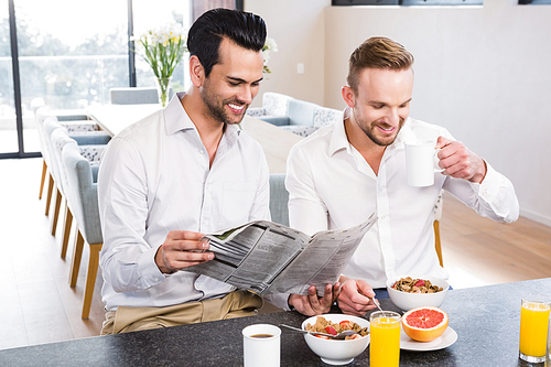 Smiling gay couple reading newspaper during breakfast