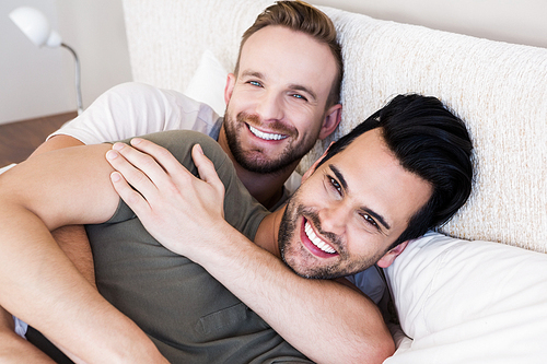 Happy gay couple lying on bed at home