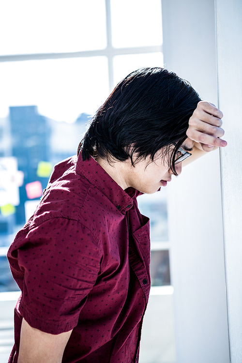 Worried creative businessman leaning on wall in office