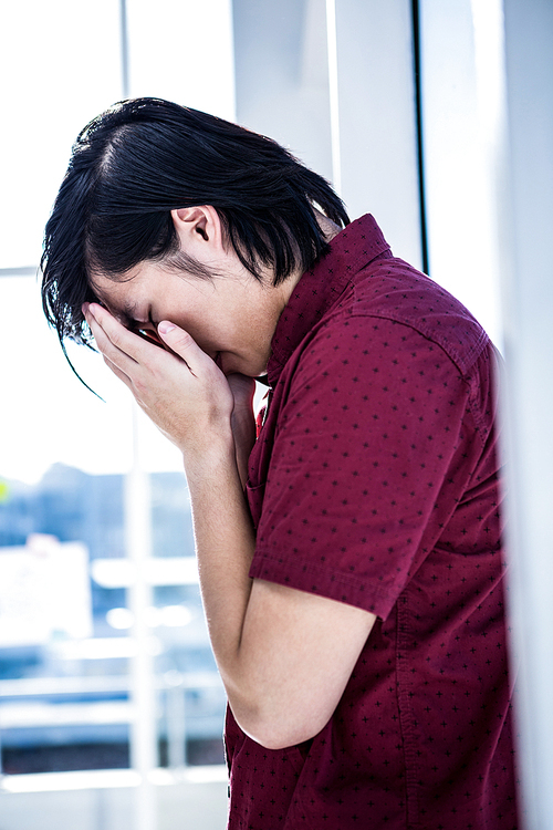 Worried creative businessman leaning on wall in office