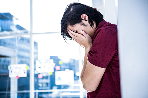 Worried creative businessman leaning on wall in office