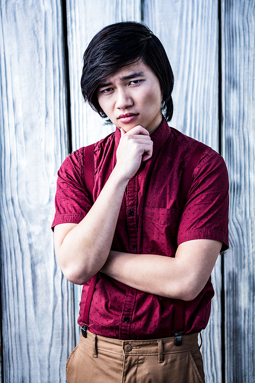 Serious hipster holding his chin on wooden background