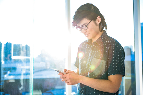 Smiling hipster using his phone in office