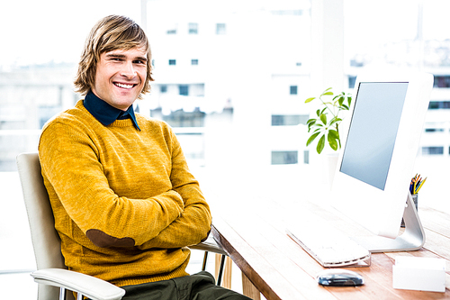 Smiling hipster businessman crossing arms in his office