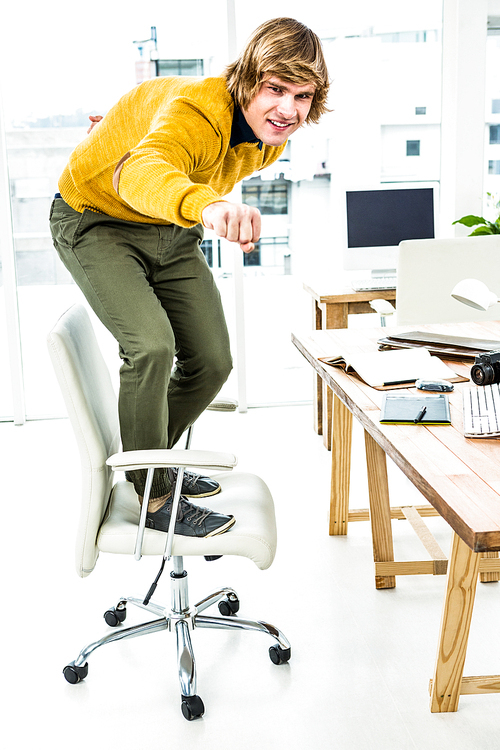 Happy hipster businessman standing on his chair in his office