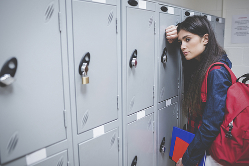 Sad student leaning on locker at university