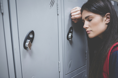 Sad student leaning on locker at university