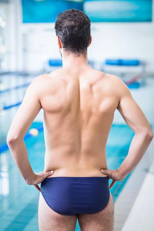 Rear view of fit man standing with hands on hips at the pool
