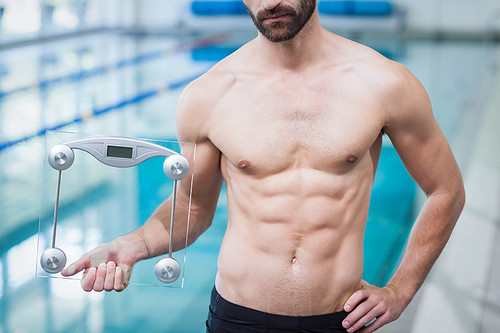 Fit man holding a weighting scale at the pool