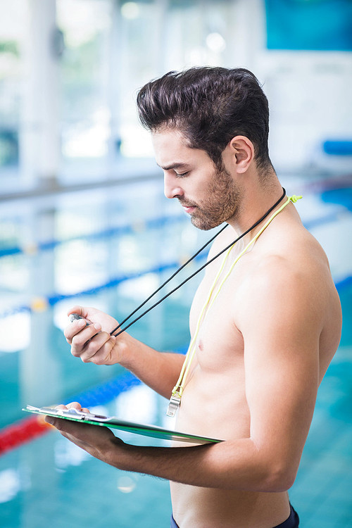 Handsome man holding clipboard and stopwatch at the pool