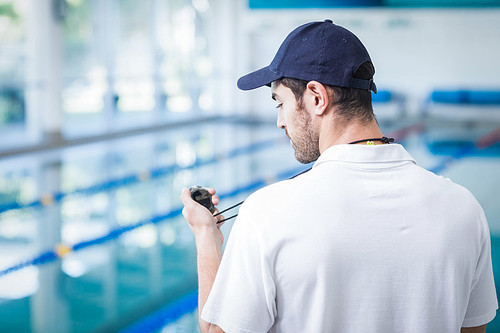 Handsome trainer looking at stopwatch at the pool