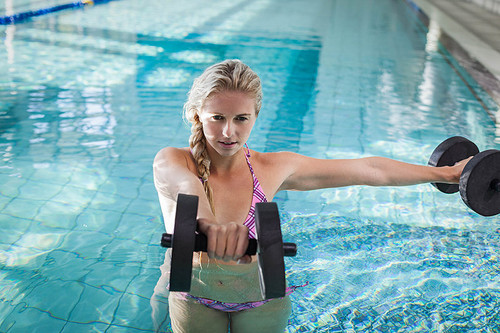 Attractive woman lifting dumbbells in the pool