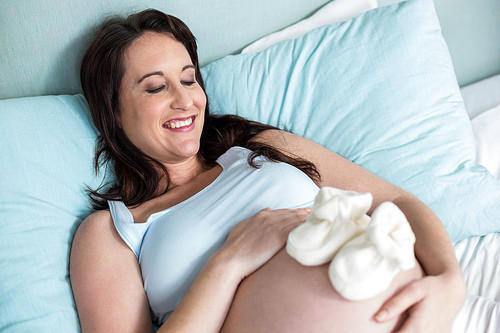 Pregnant woman with baby shoes on belly at home