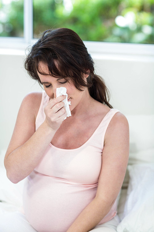 Pregnant woman sitting on bed sneezing