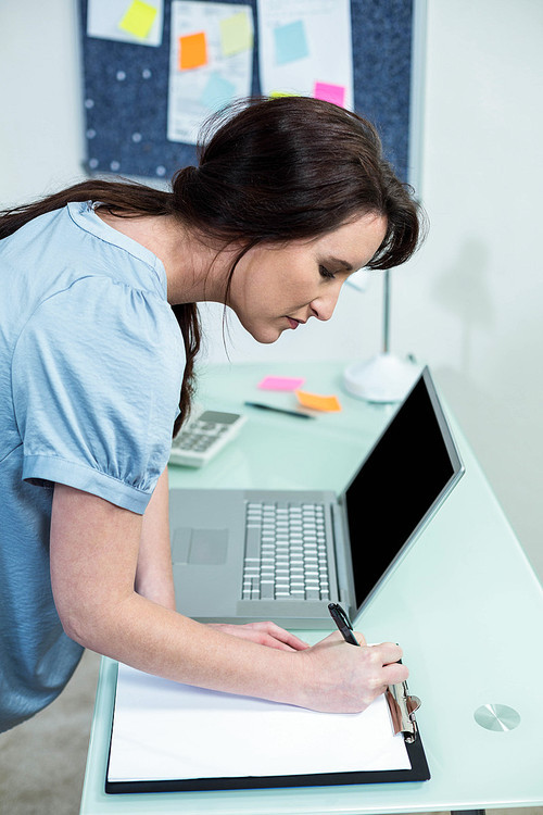 Pregnant woman writing on clipboard at desk