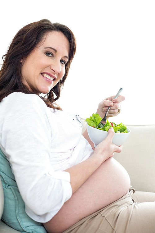 Pregnant woman eating salad on couch