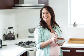 Pregnant woman eating cereal in kitchen