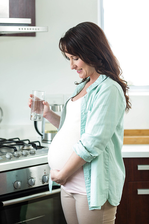 Pregnant woman holding glass of water in kitchen