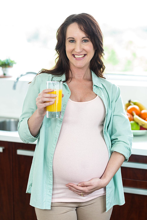 Pregnant woman holding orange juice in kitchen