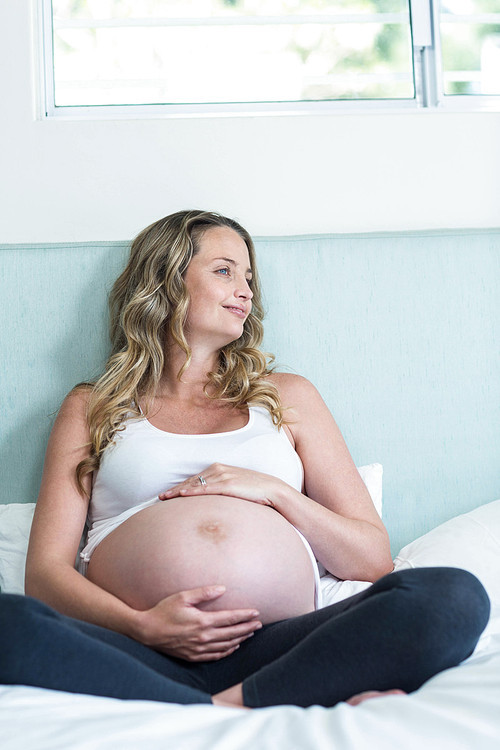 Pregnant woman touching her belly in her bedroom