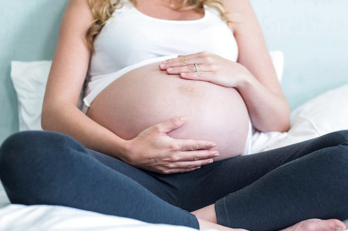 Pregnant woman touching her belly in her bedroom
