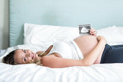 Pregnant woman showing an ultrasound picture lying on her bed