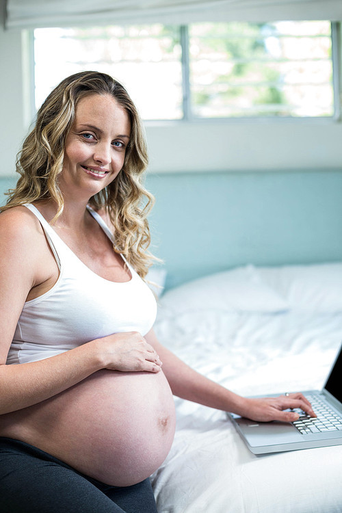 Pregnant woman using a laptop on her bed