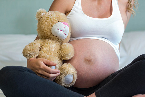Pregnant woman sitting with a teddy bear on her bed