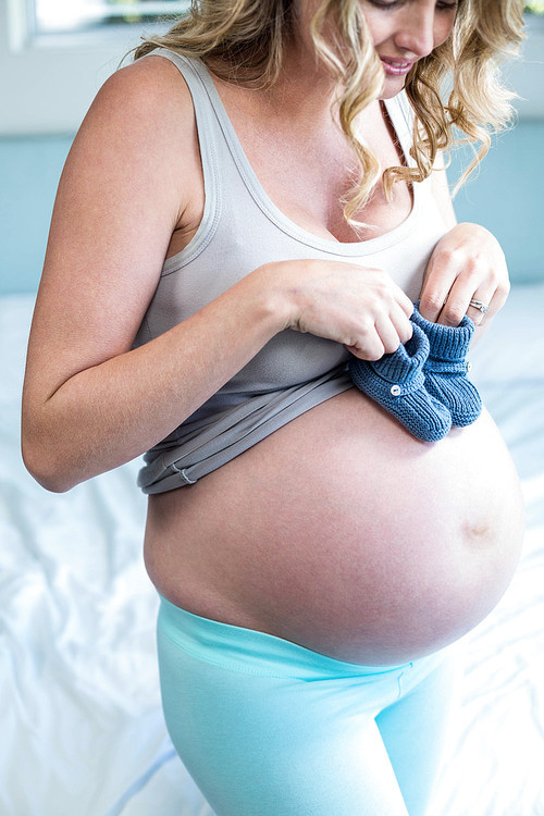 Pregnant woman with knitted slippers on her belly in her bedroom