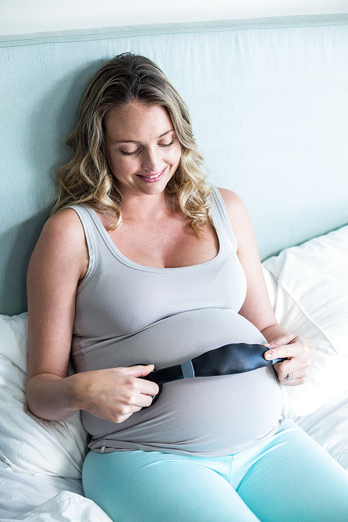 Pregnant woman making her belly listen to music in her bedroom