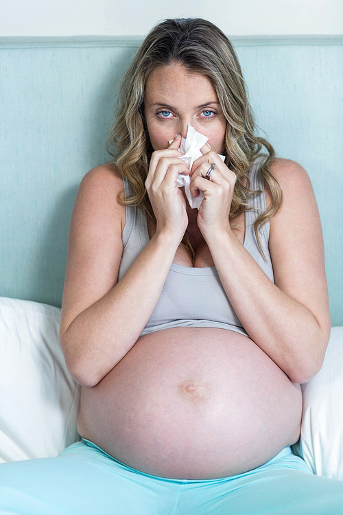 Pregnant woman blowing her nose on her bed