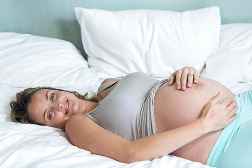 Pregnant woman lying on her bed in her bedroom