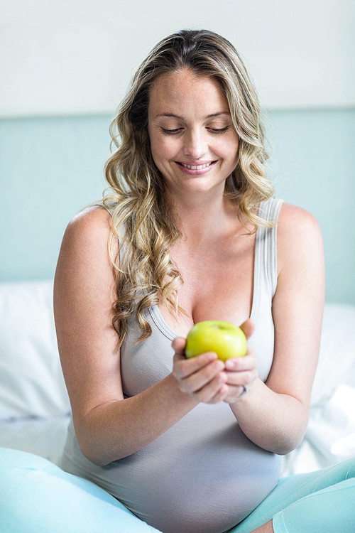 Pregnant woman holding an apple in her bedroom