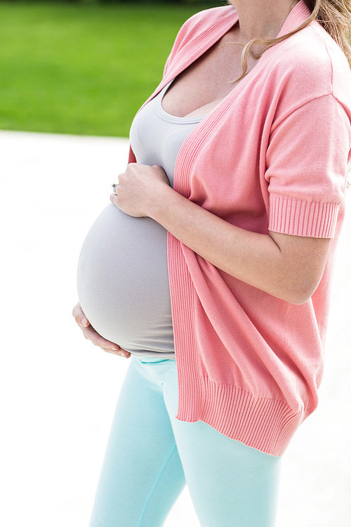 Pregnant woman touching her belly standing outside