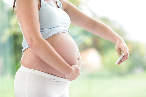 Pregnant woman taking a picture of her belly in front of a window