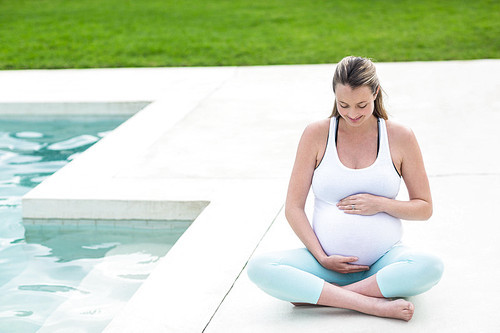 Pregnant woman touching her belly sitting next to the pool