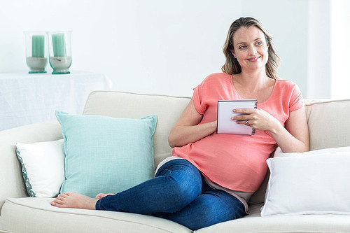 Pregnant woman writing on notepad on the couch