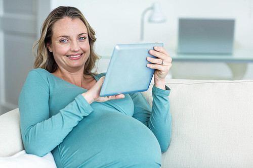 Pregnant woman using a tablet computer on the couch