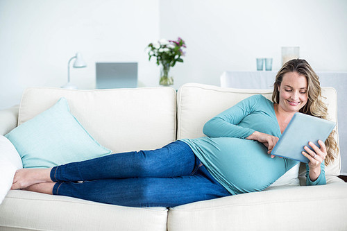 Pregnant woman using a tablet computer lying on the couch