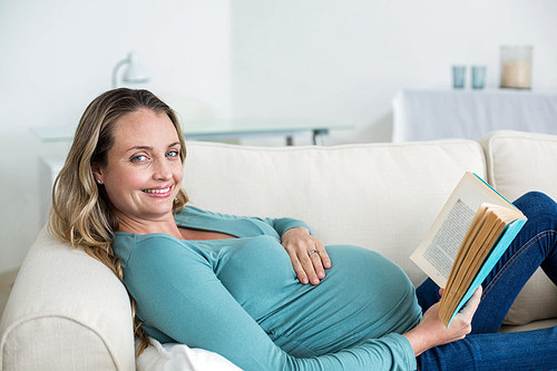 Pregnant woman reading a book lying on the couch