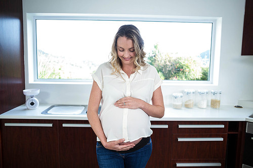 Pregnant woman touching belly in the kitchen