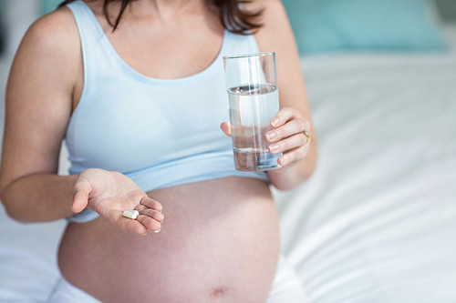 Pregnant woman taking a pill with water in her bedroom