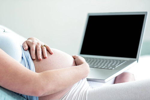 Pregnant woman using laptop in her bed