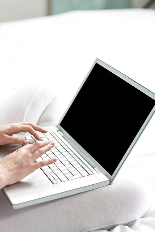 Feminine hands typing on laptop in a bedroom