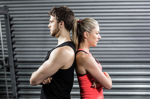 Serious couple standing back to back at crossfit gym