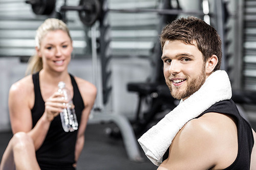 Smiling fit couple sitting at crossfit gym