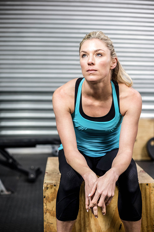 Fit woman sitting on wooden box at crossfit gym