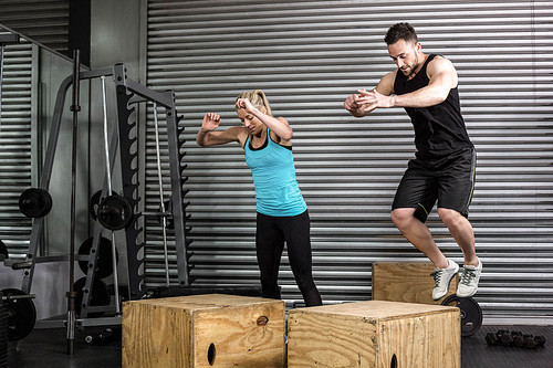 Couple doing box jumps in gym at crossfit gym