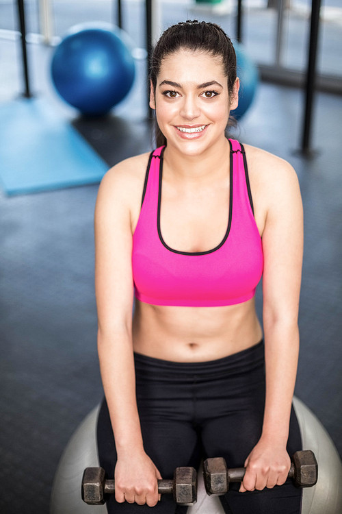 Smiling fit woman lifting dumbbells at crossfit gym